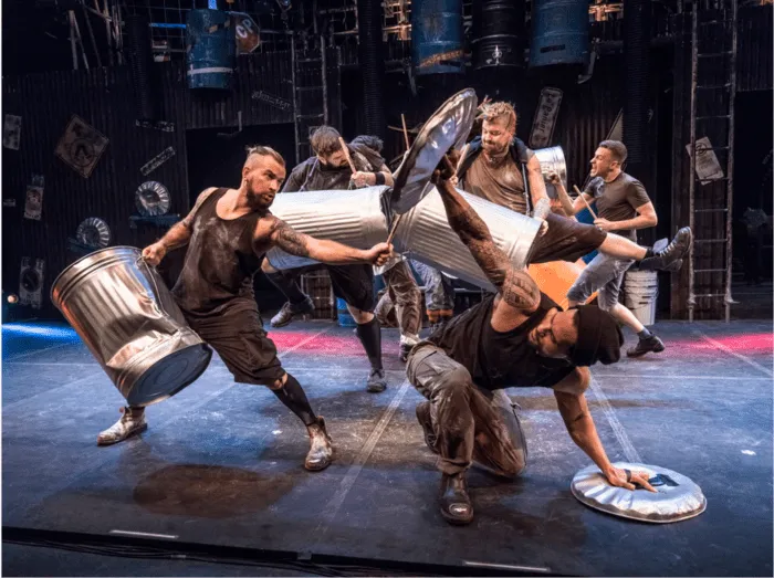 Performers in action with trash-can percussion on stage